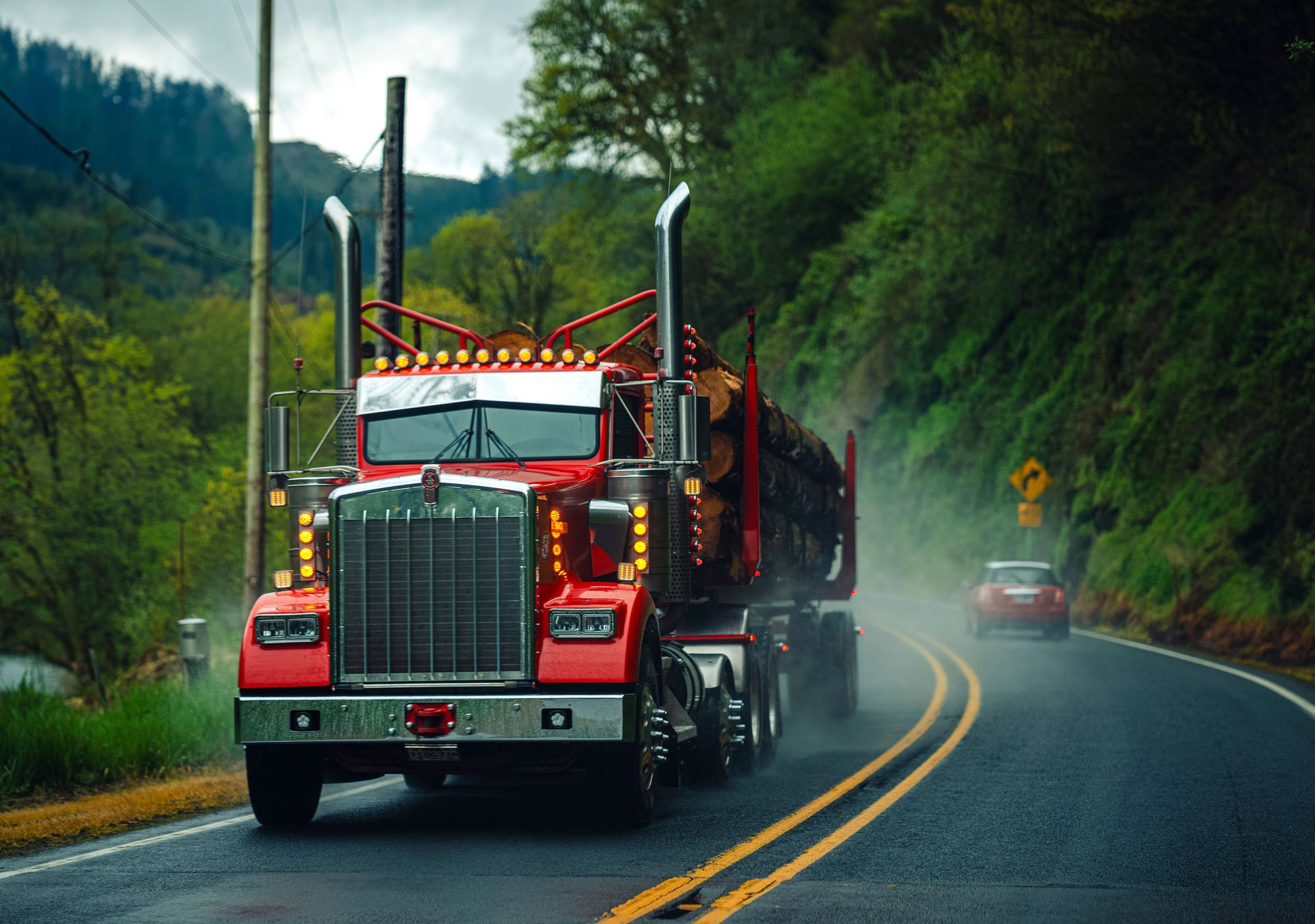 Red semi-truck carrying logs on a misty Oregon highway surrounded by lush greenery.